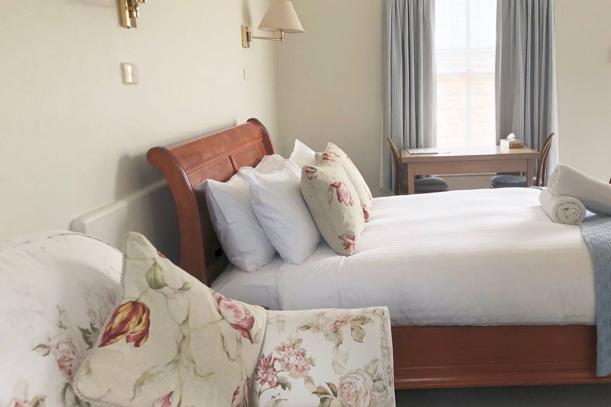A hotel room with a wooden bed, a wooden nightstand, a desk, and a floral sofa.