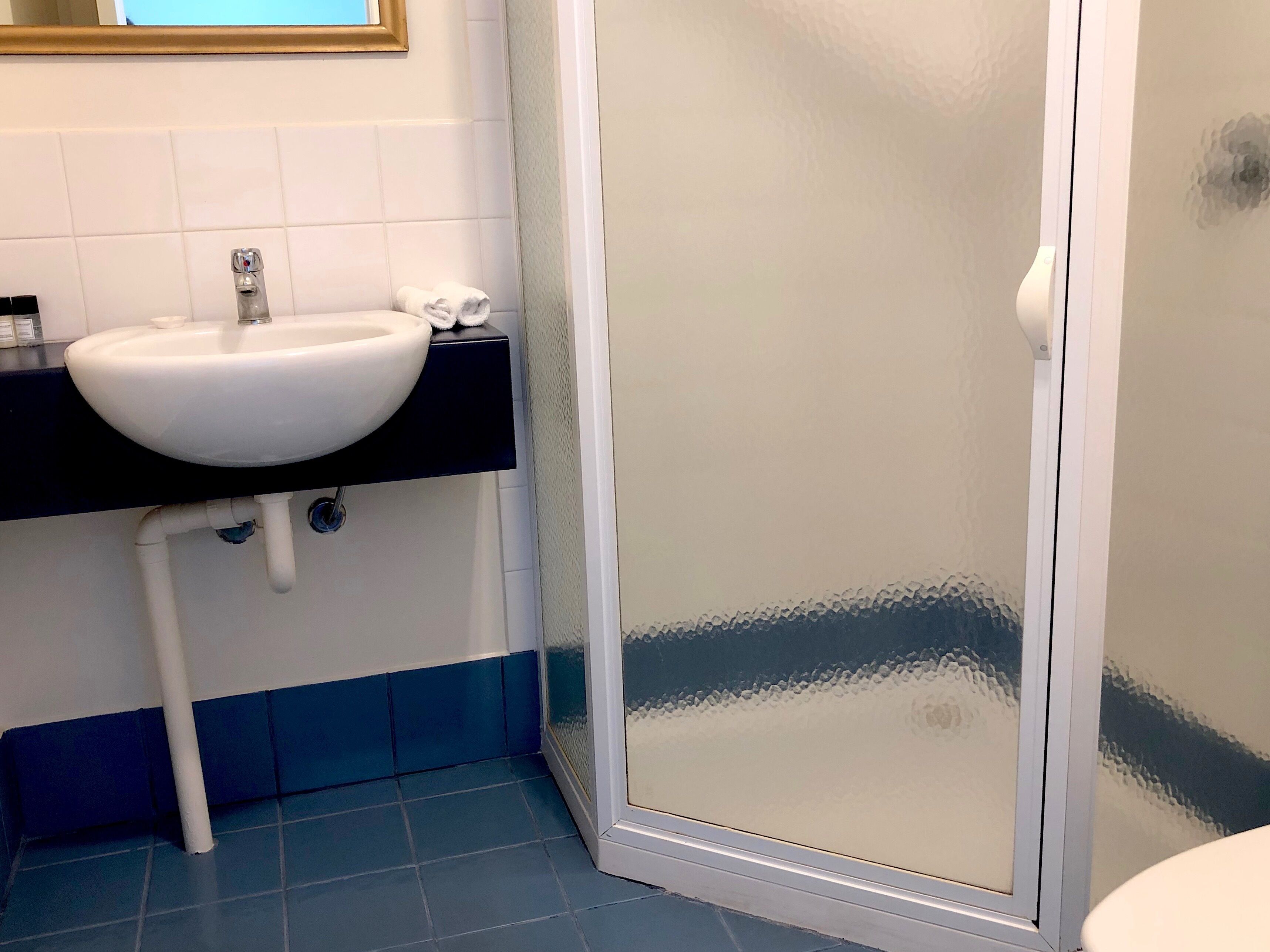 A bathroom with a white sink, black countertop, and a glass shower door.