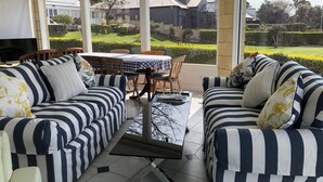 A sunlit patio with striped sofas and a table, overlooking a well-maintained garden and neighboring houses. - Douglas Riverside (Port Fairy)