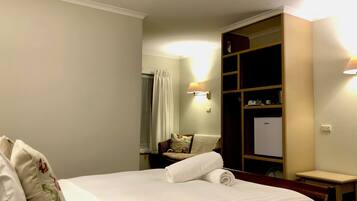 Una habitación de hotel con una cama, un armario de madera, una mesita y una lámpara de pared.
