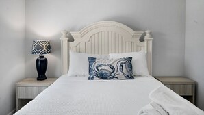 Un letto con una testiera bianca, un cuscino blu e bianco e un comodino con una lampada.