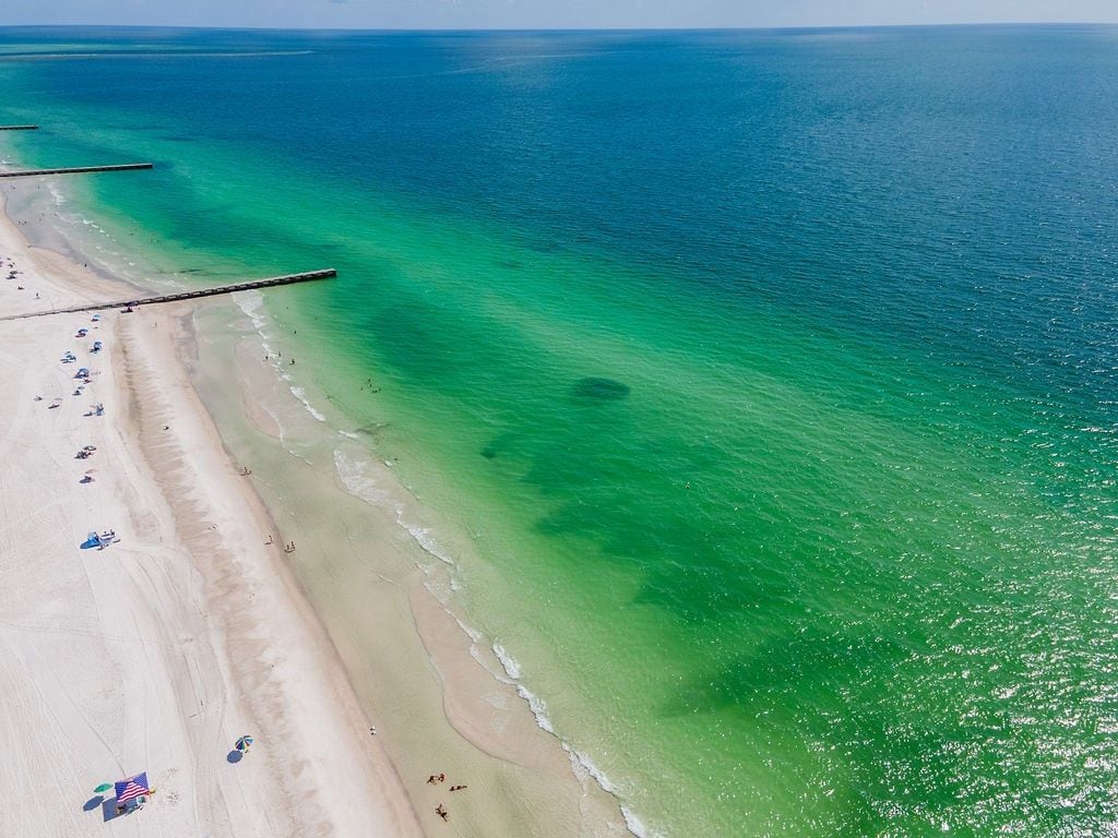 A beach with clear water, a sandy shore, and a pier extending into the sea.