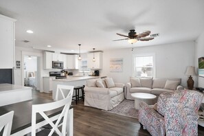 A modern kitchen with white cabinets, a microwave, and a dining area with a white table and chairs.