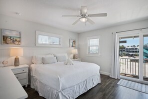 A bedroom with a bed, nightstands, a ceiling fan, and a view of the outside. - Family Tides B – AMI Retreat w/ Pool, Rooftop Deck & Gulf/Bay Views Steps To Beach (Bradenton Beach)