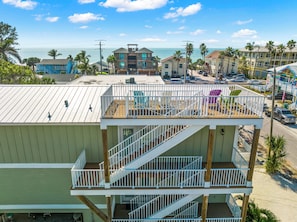 A multi-story building with a balcony and stairs, overlooking a beach and ocean. - Family Tides B – AMI Retreat w/ Pool, Rooftop Deck & Gulf/Bay Views Steps To Beach (Bradenton Beach)