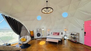 A spacious tented room with a bed, a chair, a small table, and a pink door. - Southern Boho inspired Geodesic Dome nestled up next to Big Bend National Park. (Terlingua)