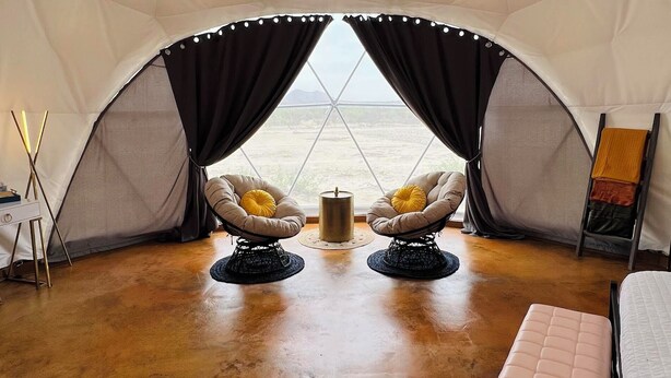 A tent with two cushioned chairs, a bench, and a hanging light fixture. - Southern Boho inspired Geodesic Dome nestled up next to Big Bend National Park. (Terlingua)