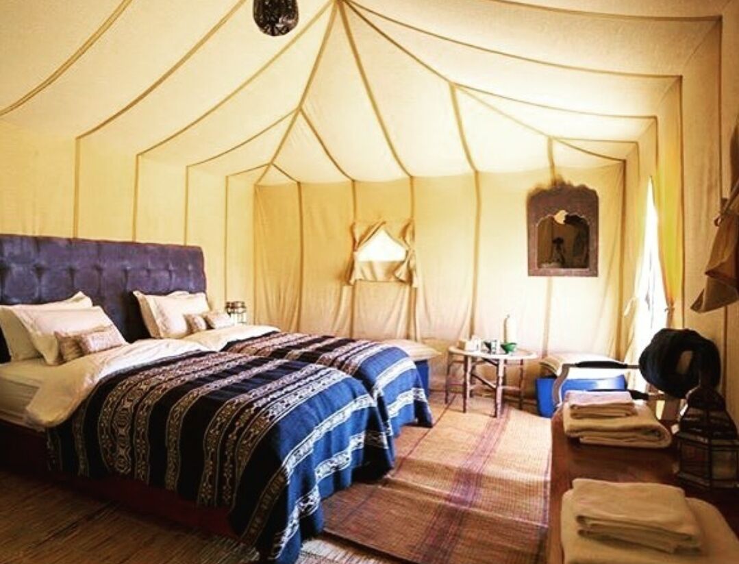 A tented room with two beds, a small table, and a lamp.