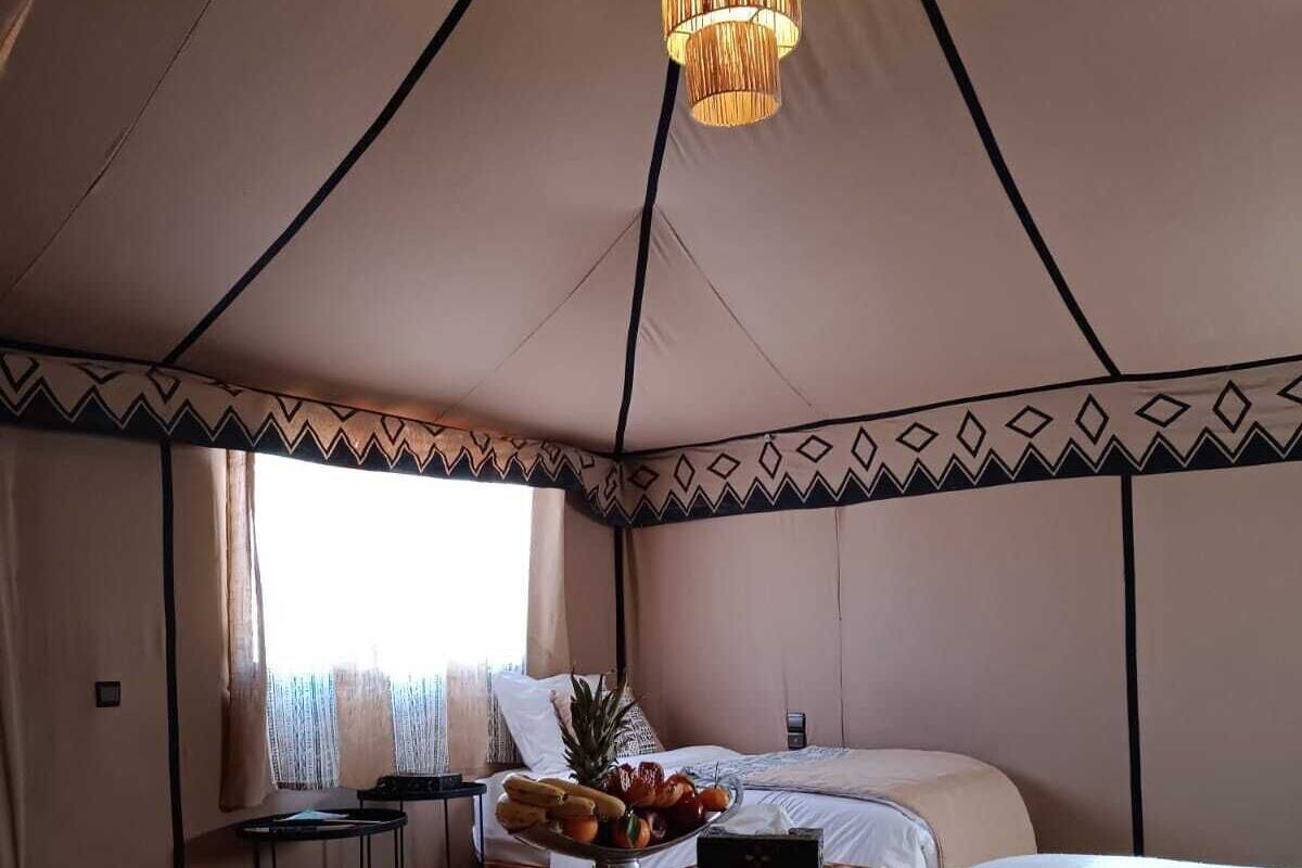 Alojamiento en tienda de campaña con cama, una mesa de comedor con fruta y una lámpara colgante.