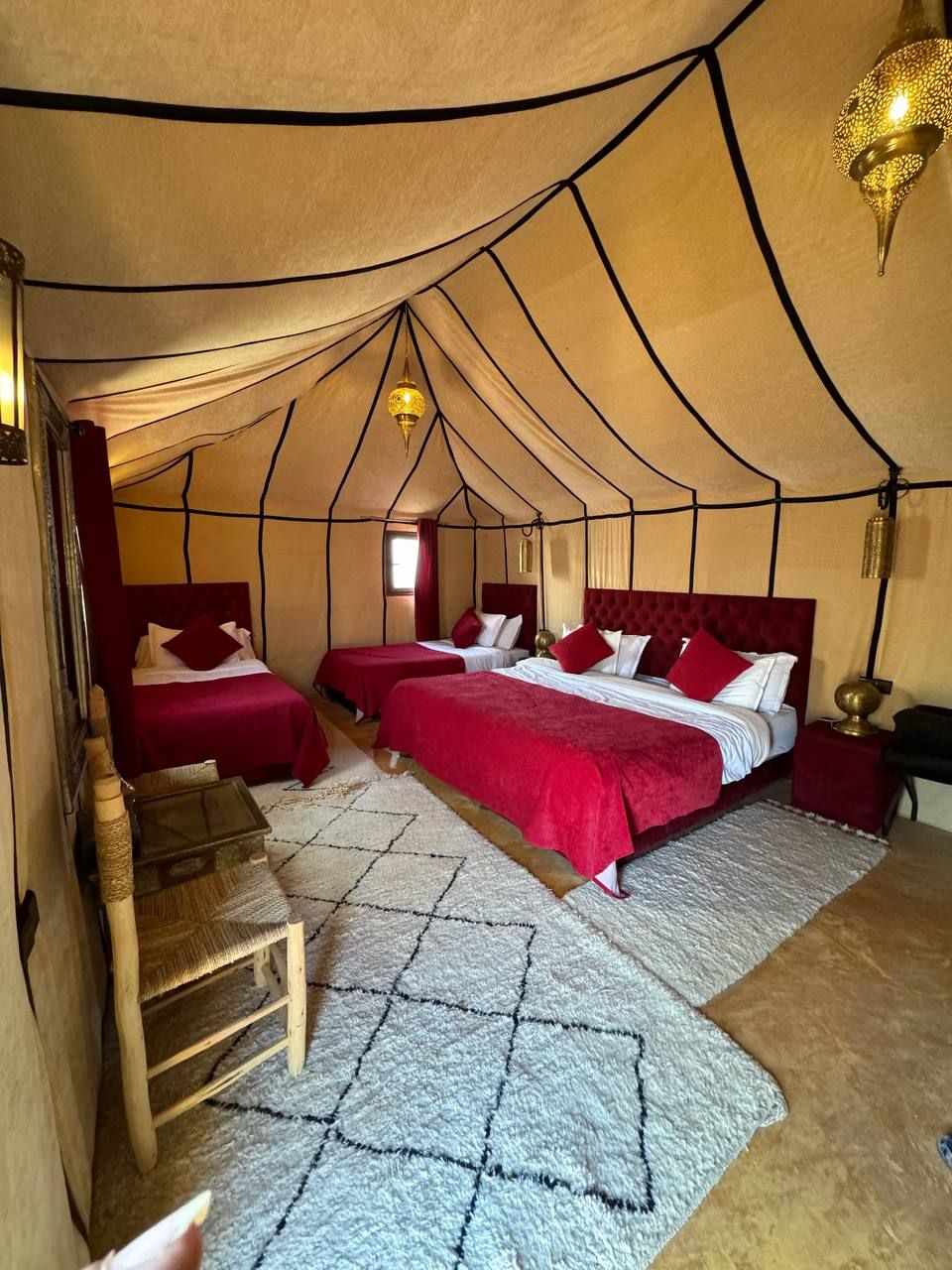 Una habitación tipo tienda con dos camas, una mesita y una lámpara colgante.