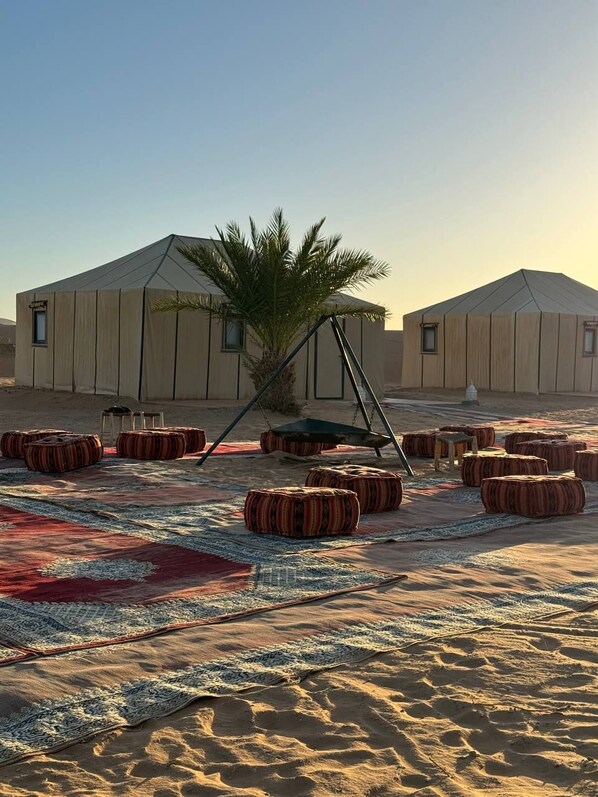 A desert camp with tents, a palm tree, and patterned rugs. - Merzouga Spirit Luxury Camp (Taouz)