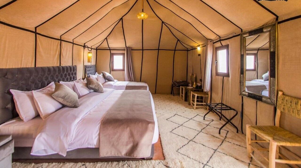 A tent with two beds, a small table, a chair, and a mirror.