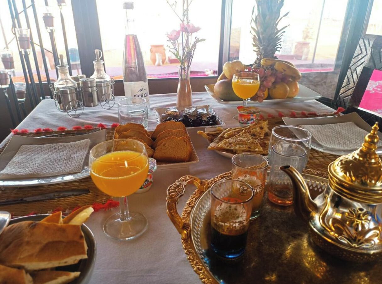 Une table mise pour le petit-déjeuner, avec une nappe et de la vaisselle pour deux personnes, comprenant du pain, des fruits et des boissons.