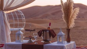 Montagem para refeições no deserto, mesa posta para dois, com sobremesa, jarra, copos e lanternas.