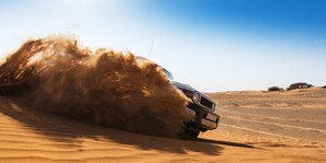 Un vehículo circulando por un desierto con dunas de arena.