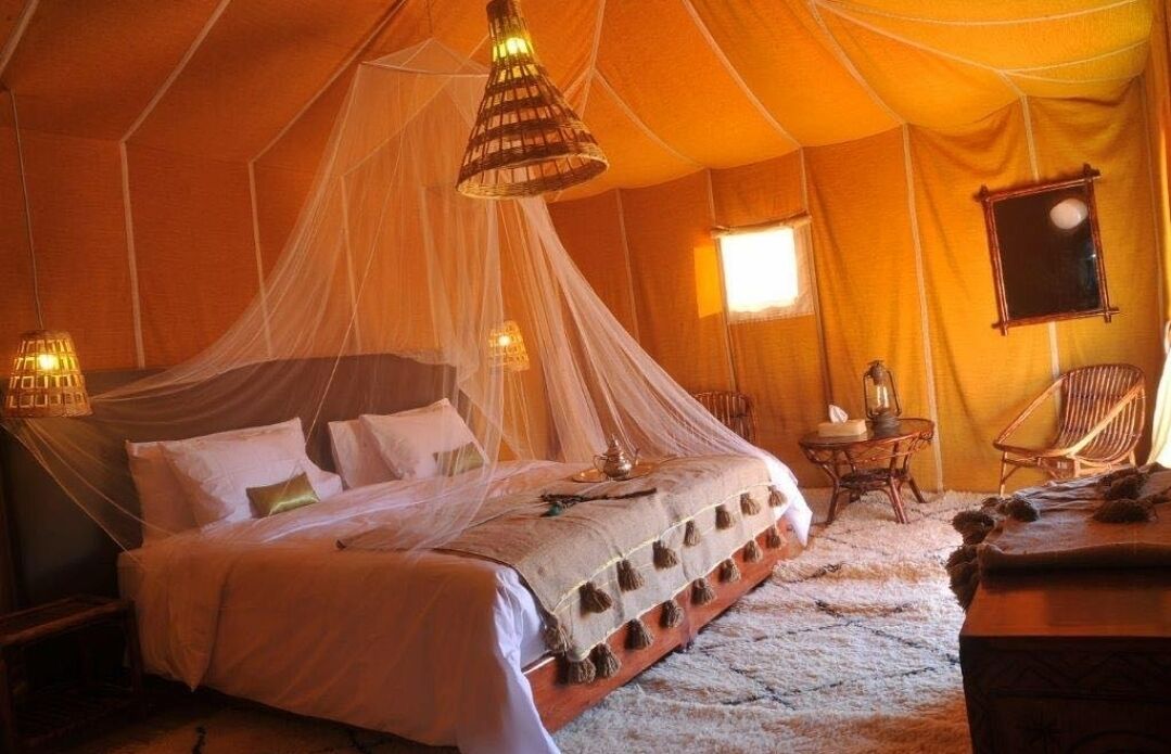Um quarto tipo tenda com cama, luminárias pendentes e uma pequena mesa.