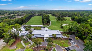 An aerial view of a golf course with a clubhouse, surrounded by lush greenery and a clear sky. - 542 Queen's Grant @ Palmetto Dunes | Dog-Friendly | Pool | Walk to Beach | Golf (Hilton Head Island)