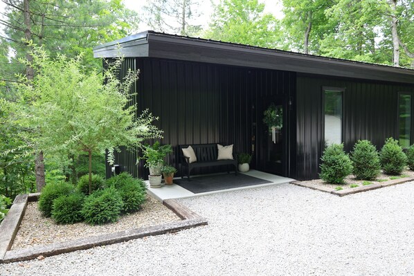 Un bâtiment moderne à la façade noire, un banc avec des coussins et des plantes en pot.