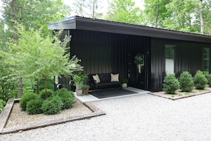 A modern building with a black exterior, a bench with cushions, and potted plants.