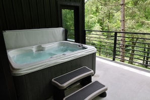 A hot tub with steps, a balcony with a railing, and a view of trees.