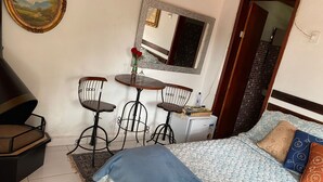 A bedroom with a bed, a desk with two chairs, a small refrigerator, and a mirror on the wall. - Recanto das Orquideas (Quatis)
