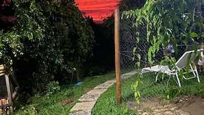 A stone pathway leading through a garden with a wire fence and a chair on the right. - Recanto das Orquideas (Quatis)