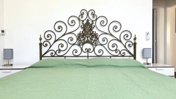 Un letto con copriletto verde, una testiera decorativa in metallo, comodini con lampade e una parete bianca.
