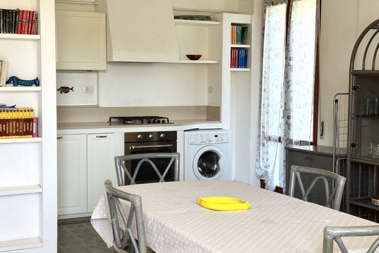 Una cucina compatta con tavolo, sedie, lavatrice e libreria.