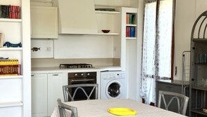 Ett kompakt kök med ett matbord, stolar, en tvättmaskin och en bokhylla.