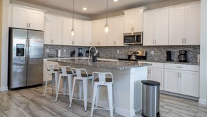 A modern kitchen with white cabinets, stainless steel appliances, a granite countertop, and pendant lighting. - Premium house with Pool BBQ just 10min to Disney (Kissimmee)