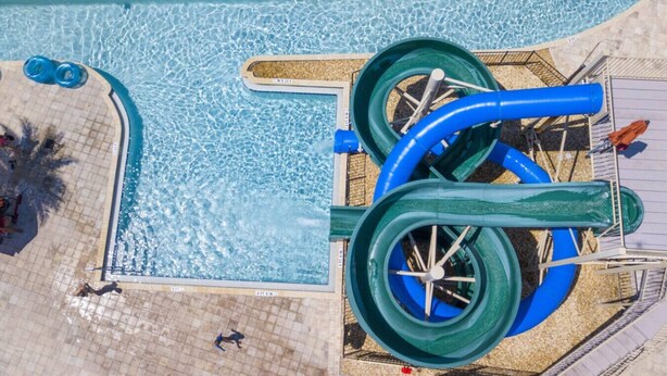 A pool with two water slides, a sandy beach area, and a few people around the pool. - Premium house with Pool BBQ just 10min to Disney (Kissimmee)
