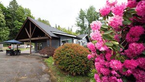 A building with a sloped roof, a covered outdoor seating area, and a well-maintained garden with flowering bushes. - Walk to Woodinville Wineries - Game Room - Fire Pit (Redmond)