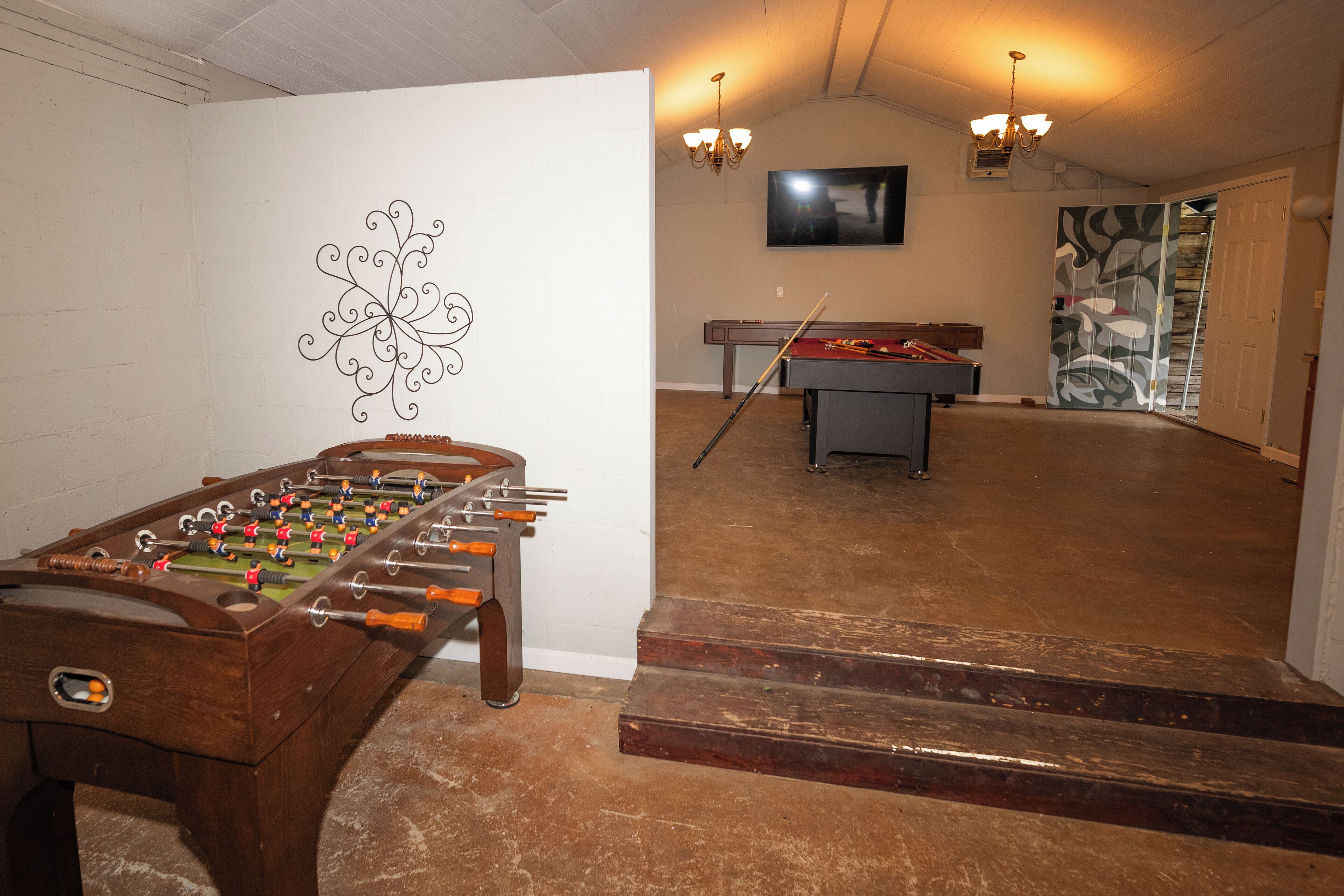 Ein Raum mit einem Kicker, einem Billardtisch und einer Treppe zu einem weiteren Bereich.