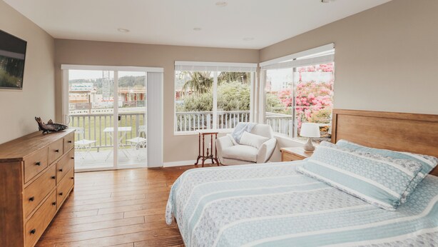 A bedroom with a large bed, a wooden dresser, a chair, and a balcony with a view of the outdoors. - Walk to Woodinville Wineries - Game Room - Fire Pit (Redmond)