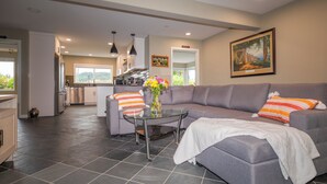A modern living room with a grey sofa, a glass coffee table, and a vase with flowers. There is a kitchen in the background with stainless steel appliances. - Walk to Woodinville Wineries - Game Room - Fire Pit (Redmond)