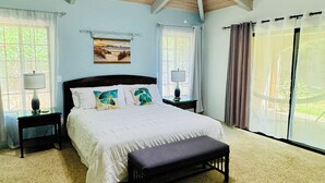 A bedroom with a wooden ceiling, a bed with white bedding, a bench, two bedside tables with lamps, and a large window with curtains.