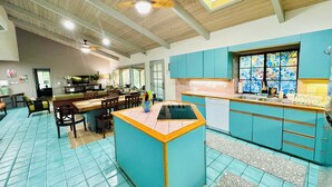 A spacious kitchen with teal cabinetry, a central island, and a ceiling fan.