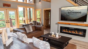 A spacious living room with a fireplace, leather sofas, and a large TV screen displaying 'tennessee'. - 3410 sq ft Very Large-Pool Community cabin, Mountain Views-4 King beds-POOL tble (Pigeon Forge)