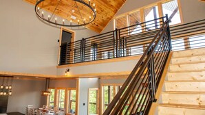 A spacious interior with a high ceiling, a staircase with a metal railing, and large windows allowing natural light. - 3410 sq ft Very Large-Pool Community cabin, Mountain Views-4 King beds-POOL tble (Pigeon Forge)