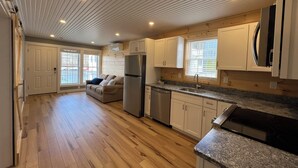 A spacious kitchen with wooden flooring, white cabinets, a stainless steel refrigerator, and a granite countertop. - Spectacular Sunset Suite (Laconia)