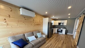A compact living space with a kitchenette, a sofa with cushions, and a wooden floor. - Spectacular Sunset Suite (Laconia)