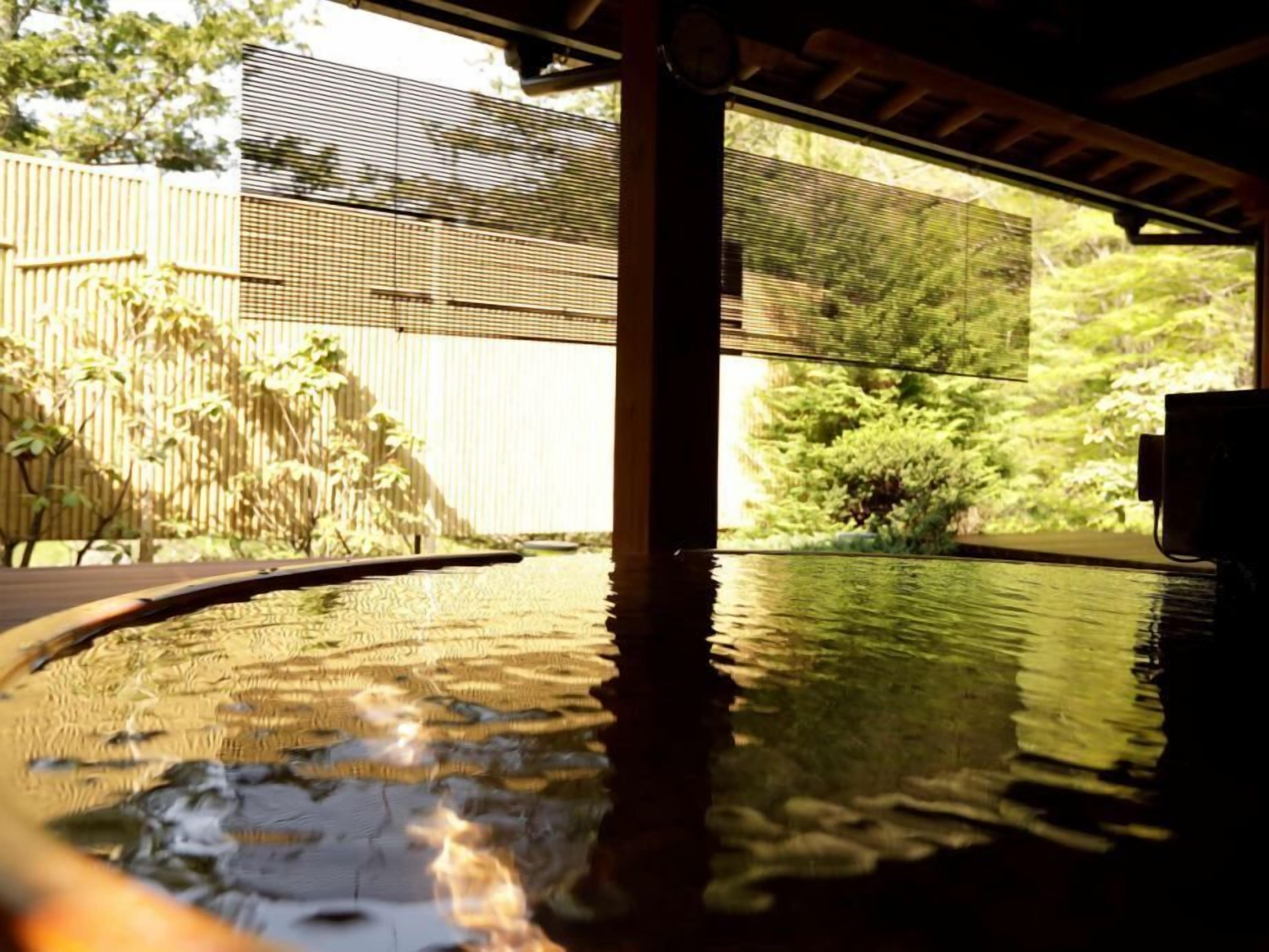 A pool area with a wooden deck, a bamboo fence, and a view of greenery.