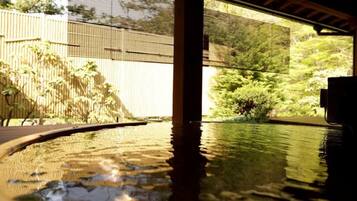 A pool area with a wooden deck, a bamboo fence, and a view of greenery.