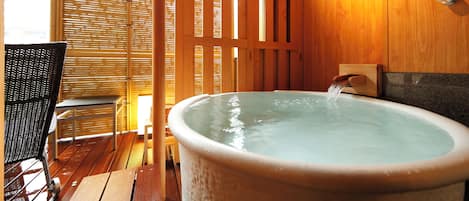 Un jacuzzi con piso de madera y una pantalla de bambú al fondo.