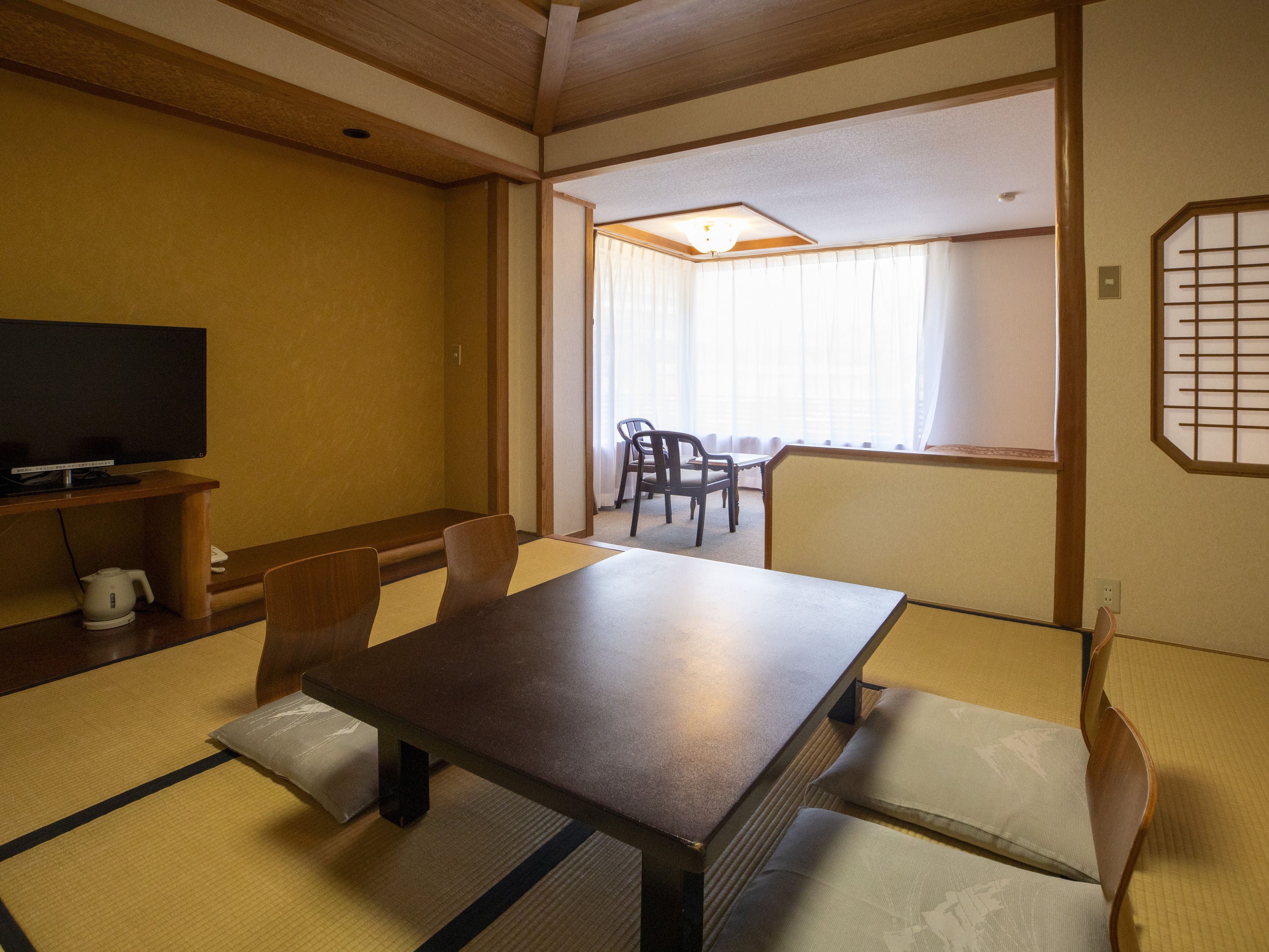 A traditional Japanese room with tatami flooring, a low table, and a television on a stand.
