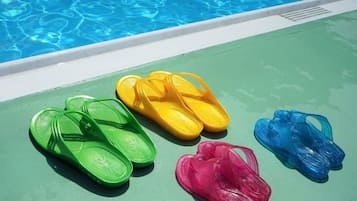 A poolside area with a green surface and four pairs of flip-flops in green, yellow, pink, and blue colors.