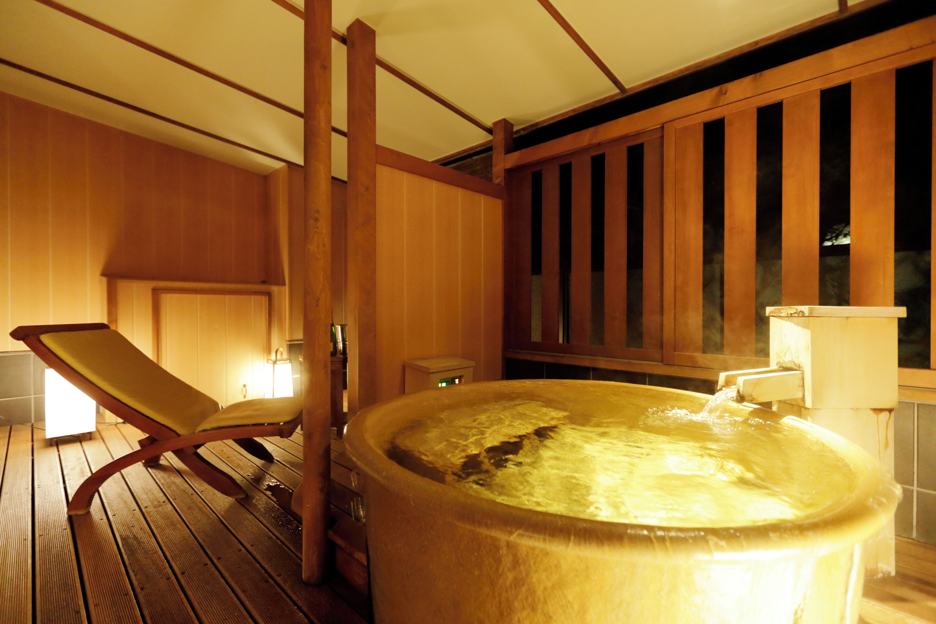 A wooden deck with a hot tub, a lounge chair, and a wooden wall with vertical slats.