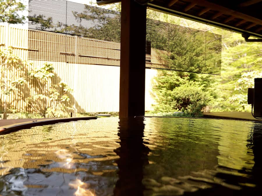 Une piscine avec une terrasse en bois et une clôture en bambou en arrière-plan.