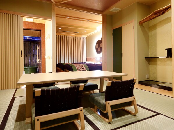 Una habitación con suelo de tatami, una mesa baja, dos sillas, un sofá y una puerta corredera que da a un baño.