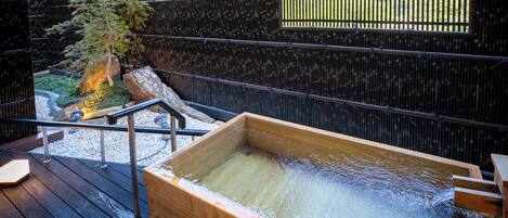 A wooden hot spring bath area with a wooden deck, metal railings, and a bamboo tree.